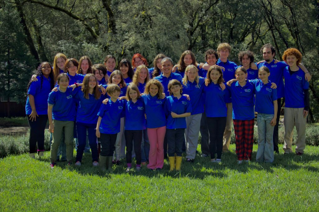 Kairos singers stand smiling in a green field, wearing blue t shirts.